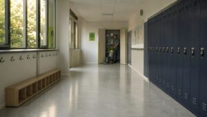 Couloir d'ecole elementaire fraichement nettoyée en Val d'Oise — sol PVC clair brillant, casiers metalliques bleu marine, autolaveuse en action au fond